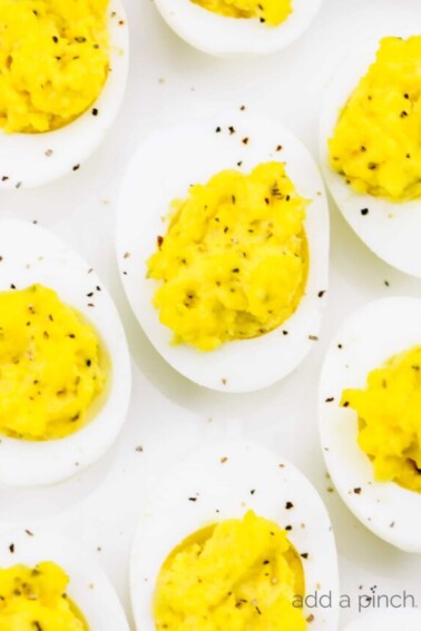 Closeup photograph of deviled eggs sprinkled with black pepper on a white platter.