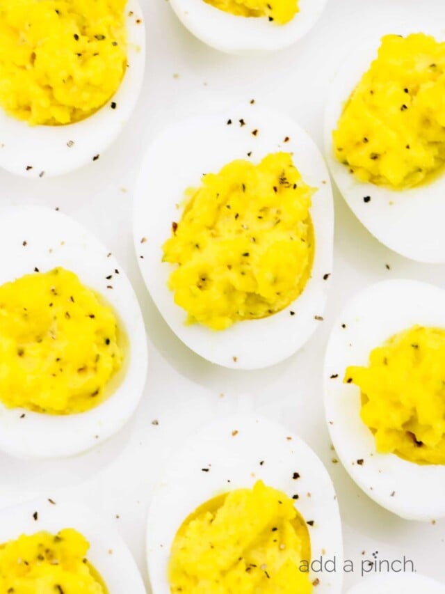 Closeup photograph of deviled eggs sprinkled with black pepper on a white platter.