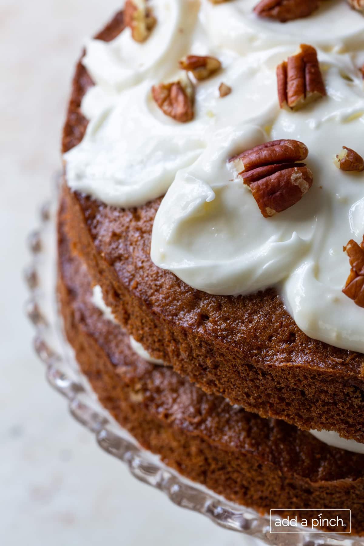 Photo of carrot cake topped with cream cheese frosting and toasted pecans.