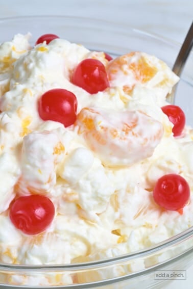 Ambrosia salad with cherries in a clear glass bowl.
