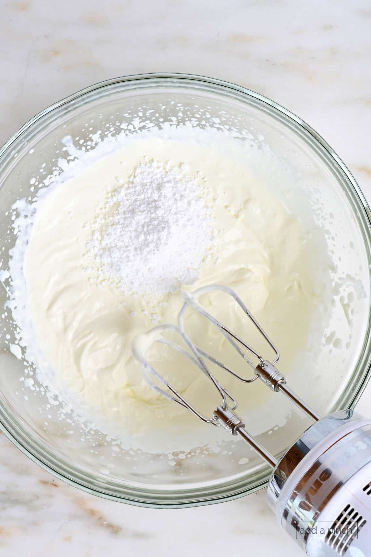 Lightly whipped cream and confectioner's sugar in a glass mixing bowl.