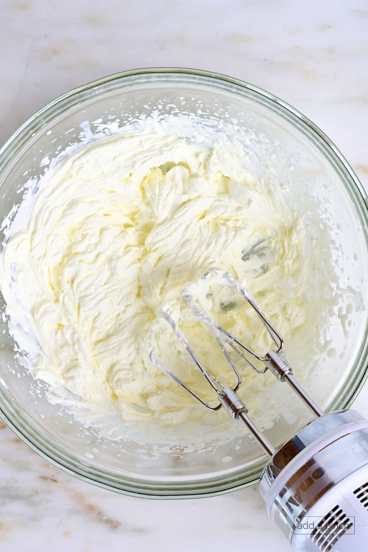 Whipped cream in a mixing bowl with hand mixer.