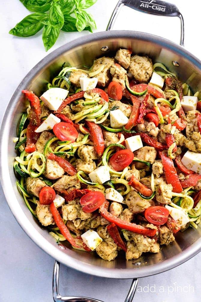One Pan Pesto Chicken Recipe - This One Pan Pesto Chicken recipe makes a quick and easy answer to what's for supper? Made with chicken, pesto, peppers, tomatoes, zucchini and mozzarella, this will easily become a favorite! // addapinch.com
