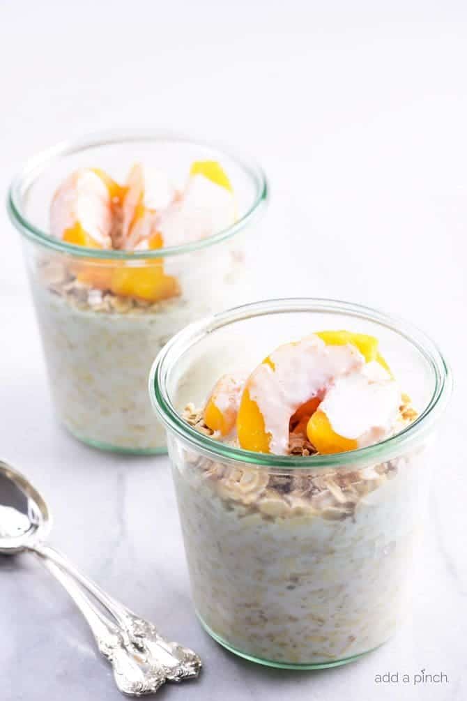 Peaches and Cream Overnight Oats in glass jars, with silver spoons. // addapinch.com