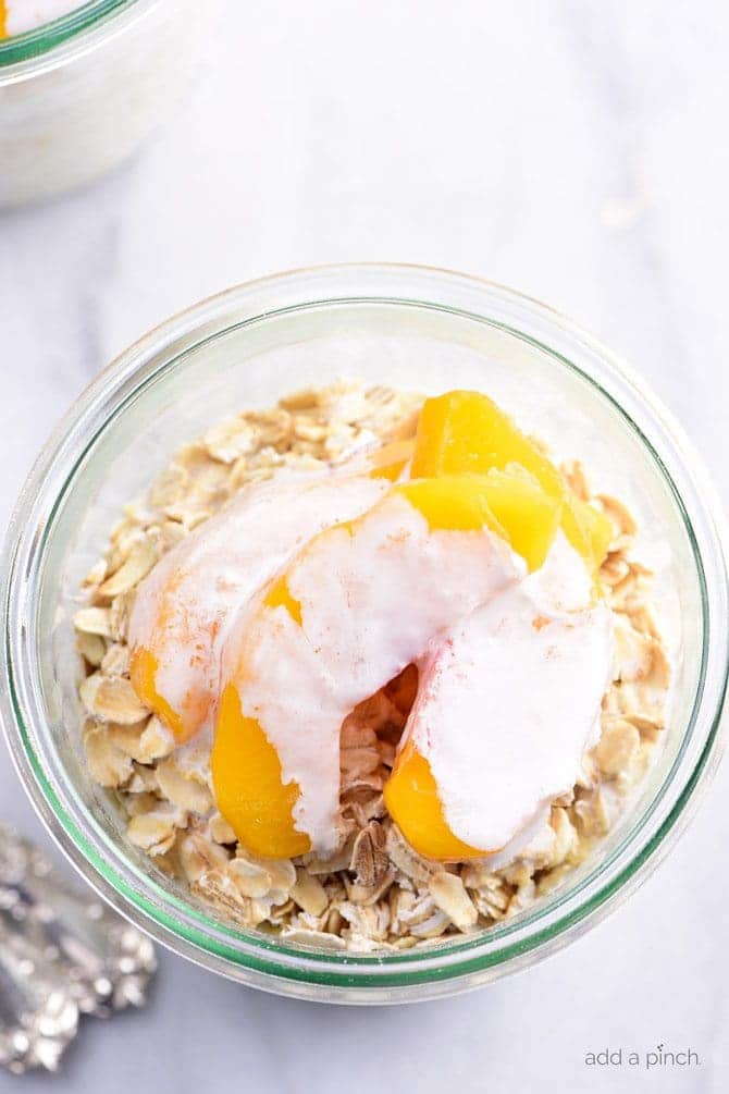 Overhead picture of overnight oats with peaches and drizzle of heavy cream in a glass jar // addapinch.com