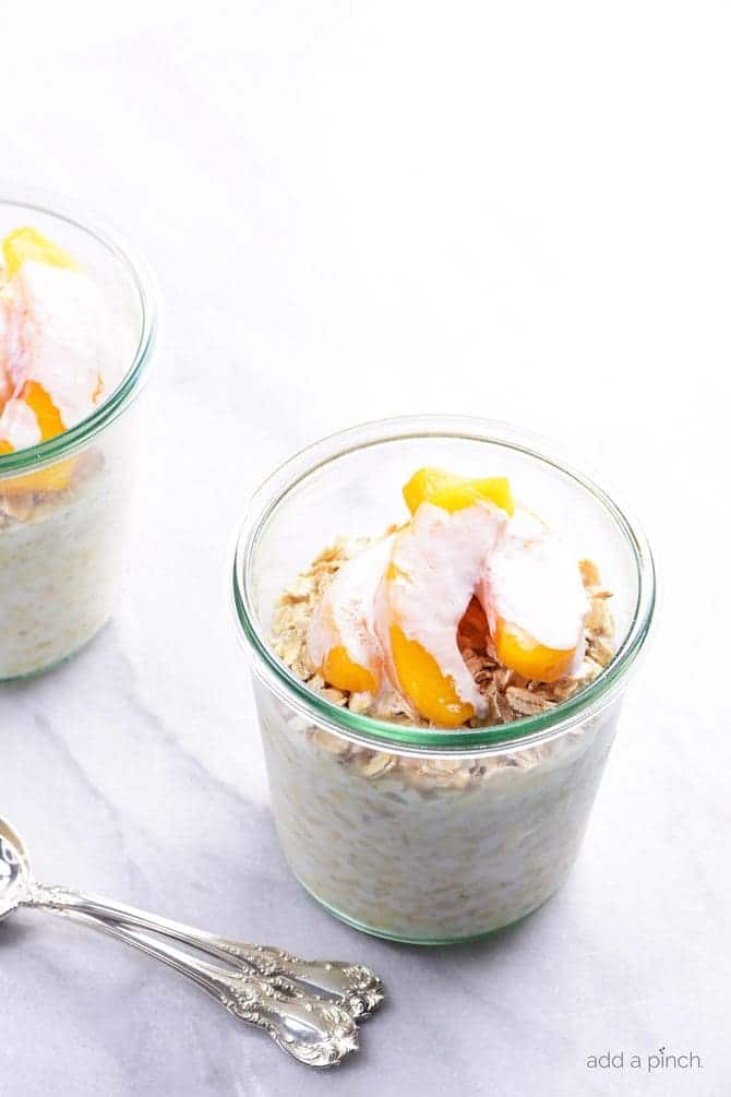Two jars of overnight oats with peaches, cream and a silver spoon on a marble countertop // addapinch.com