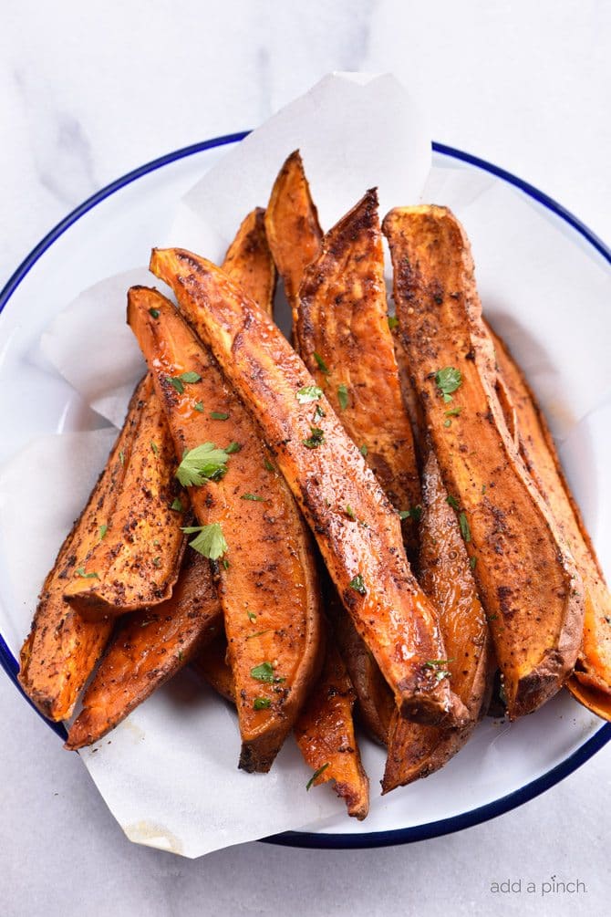 Baked sweet potato wedges coated with spices and fresh green herbs on a white plate with blue rim. 