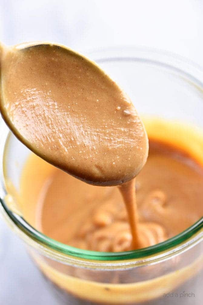 Spoon of peanut sauce drizzling it back into a jar.  // addapinch.com