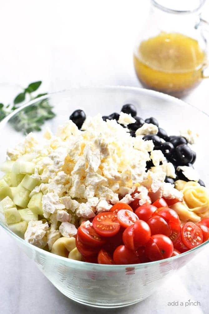 Ingredients for Tortellini Pasta Salad -cucumbers, tomatoes, feta cheese and black olives - in glass bowl // addapinch.com