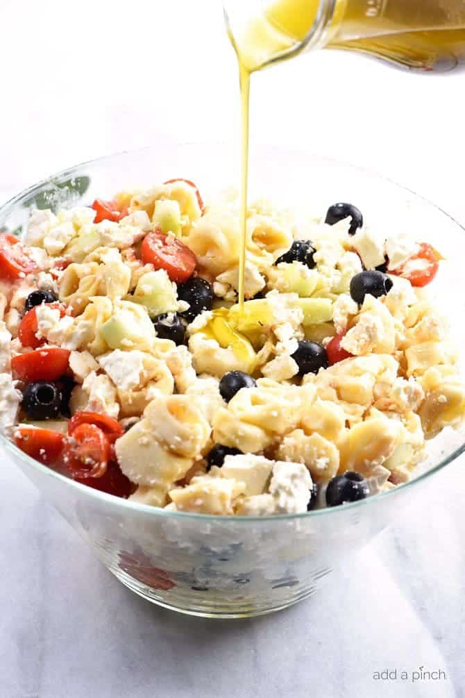 Ingredients for Tortellini Pasta Salad combined well and being drizzled with homemade Italian Dressing from glass dispenser. // addapinch.com