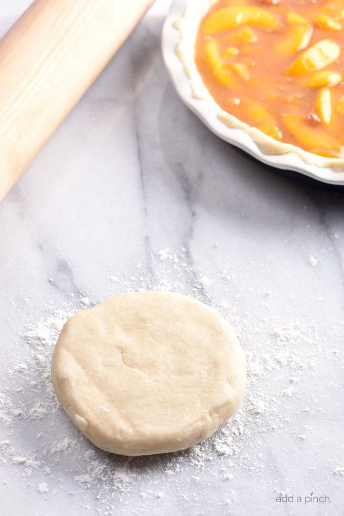 pie crust dough on a flour dusted marble surface with a wooden rolling pin and pie plate in the background.