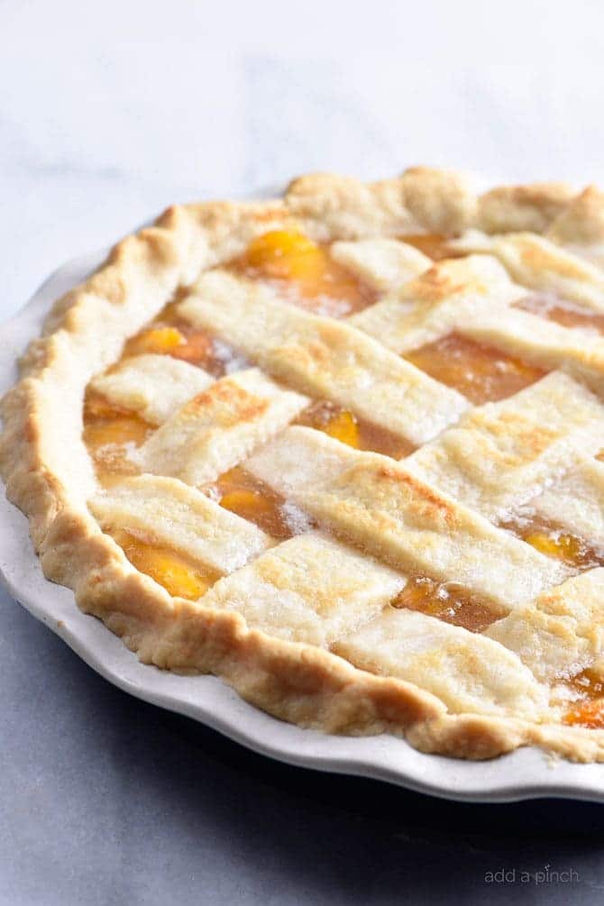 Baked lattice topped peach pie in a white pie plate on a marble surface.
