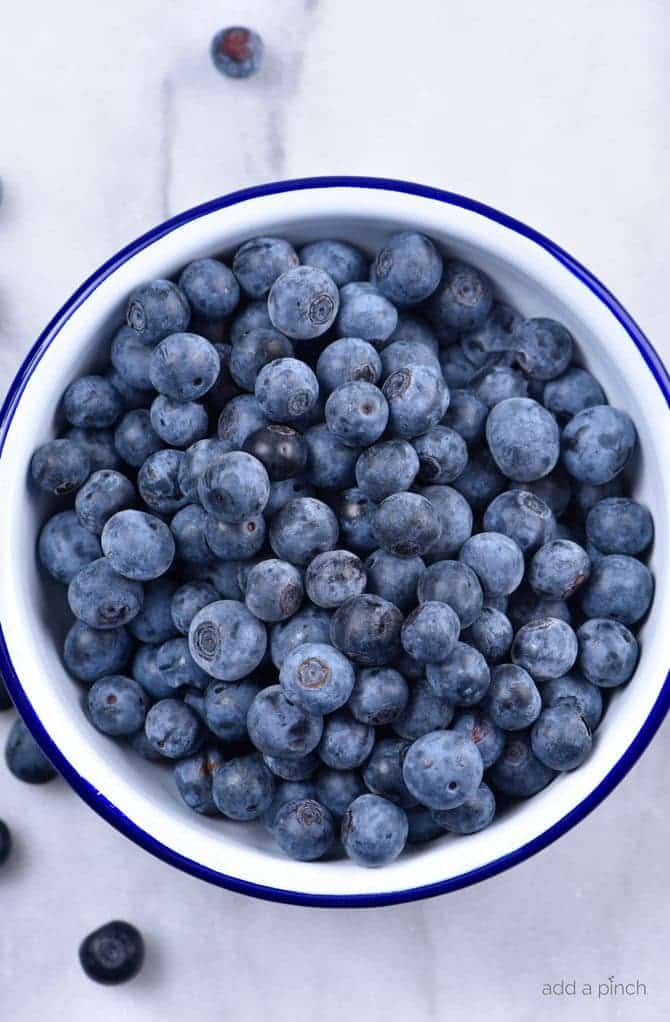 Fresh ripe blueberries in white enamel bowl with blue rim, set on marble counter // addapinch.com