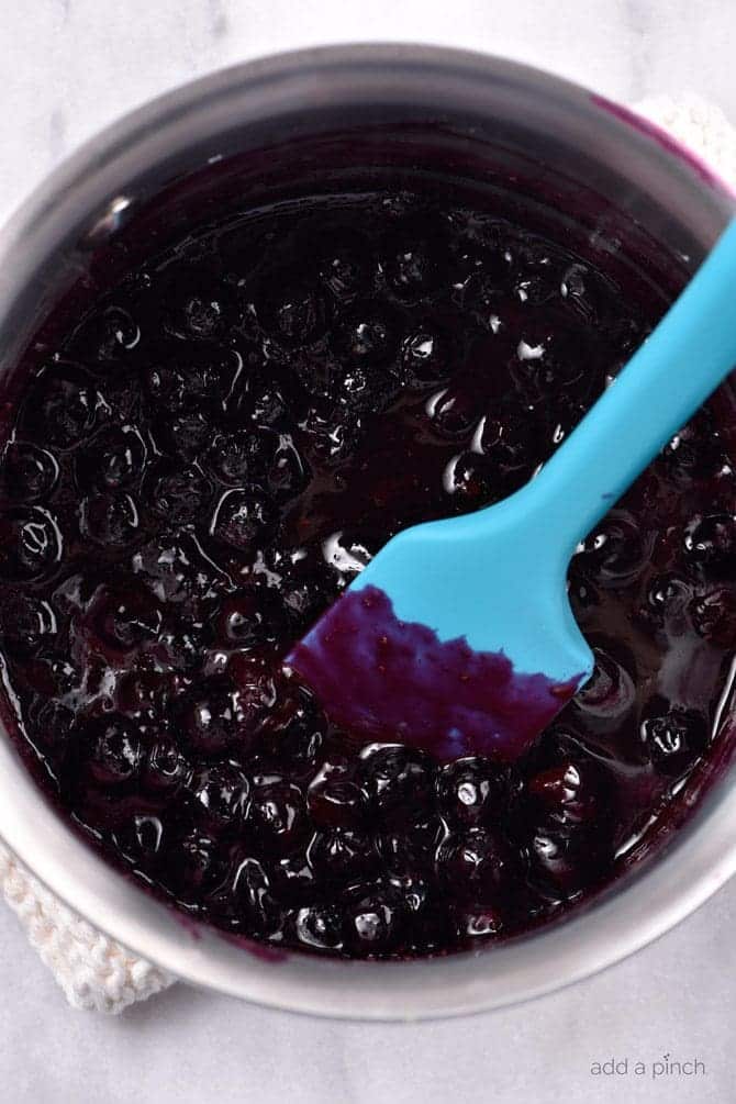 Blue spatula stirring pot of blueberry sauce// addapinch.com
