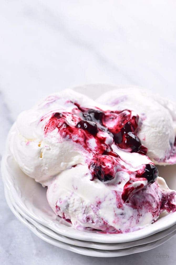 Scoops of Blueberry Cheesecake Ice Cream with blueberries swirled on top, in a white bowl. // addapinch.com
