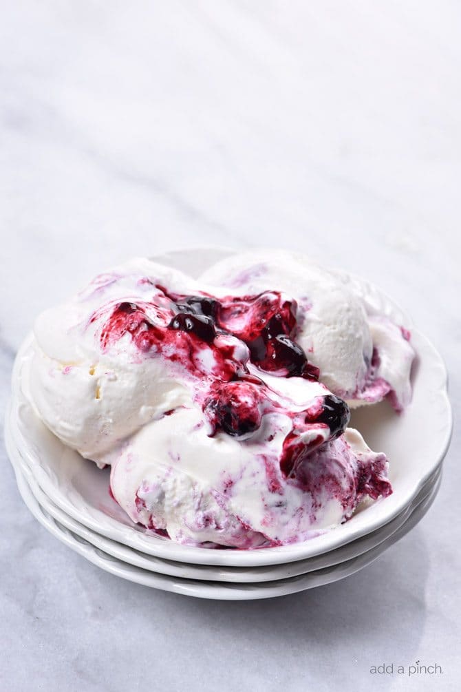 Scoops of Blueberry Cheesecake Ice Cream showing blueberry sauce on top, in a white bowl on white marble counter // addapinch.com