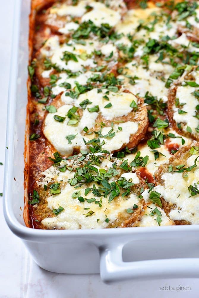 White baking dish with eggplant, cheeses, sauce and fresh herbs. 