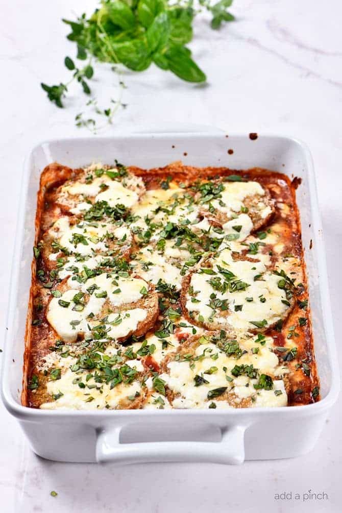 Baking dish with eggplant topped with parmesan surrounded by fresh basil. 
