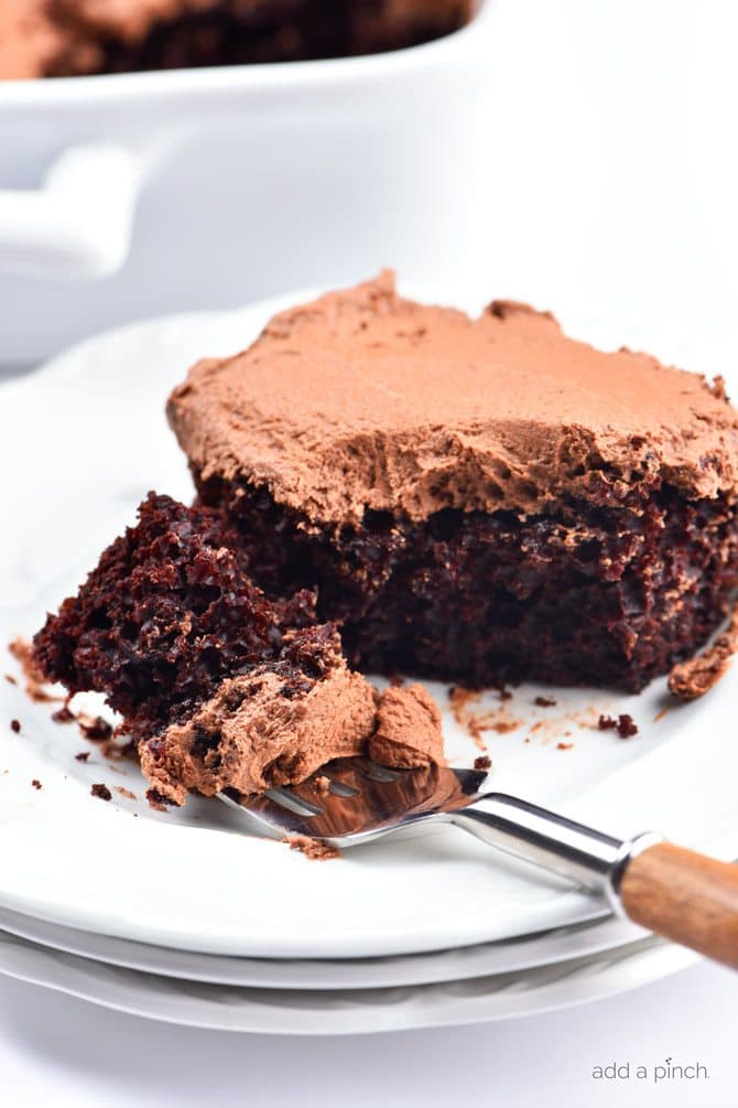 Bite from a piece of 9x13 chocolate cake on a fork on a stack of white plates.