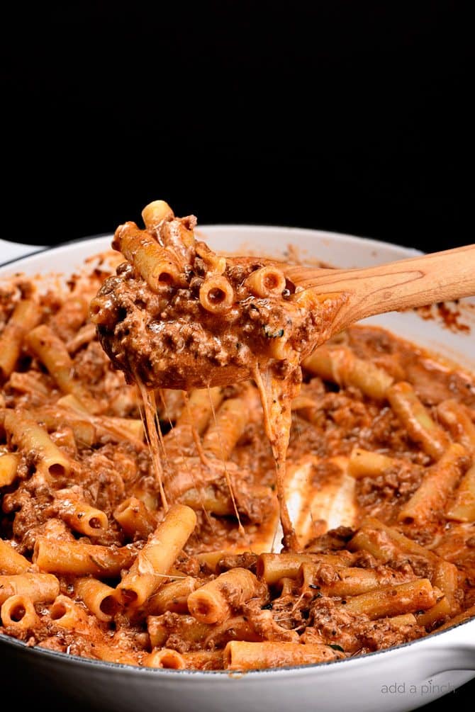 Skillet Beef Ziti in skillet with wooden spoon and cheese pull - addapinch.com