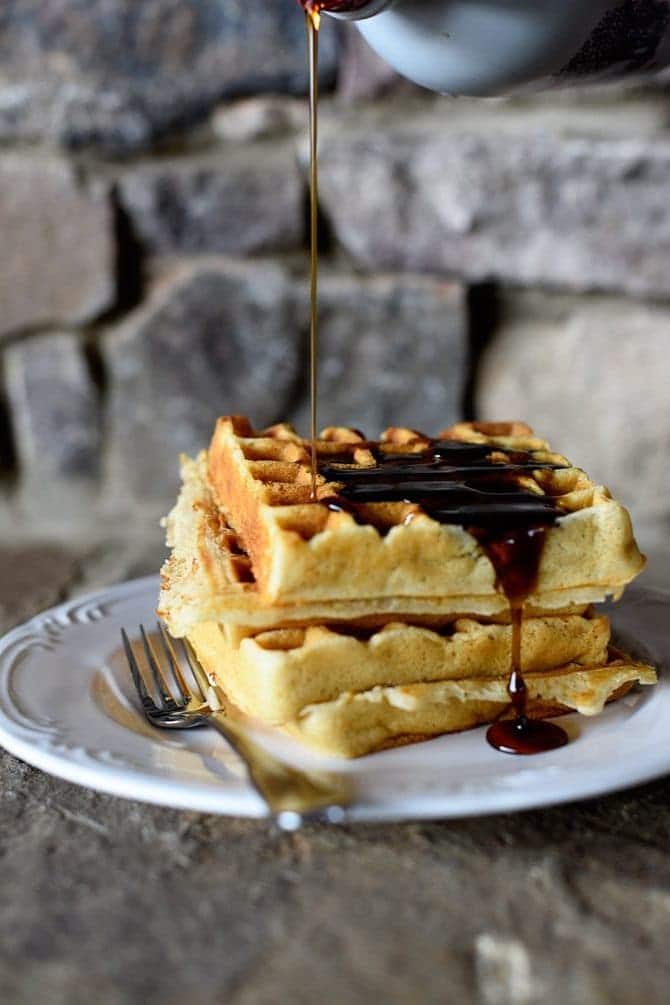 Our favorite buttermilk waffles are golden and crisp on the outside and drizzled with syrup. Served on white plate with fork. // addapinch.com