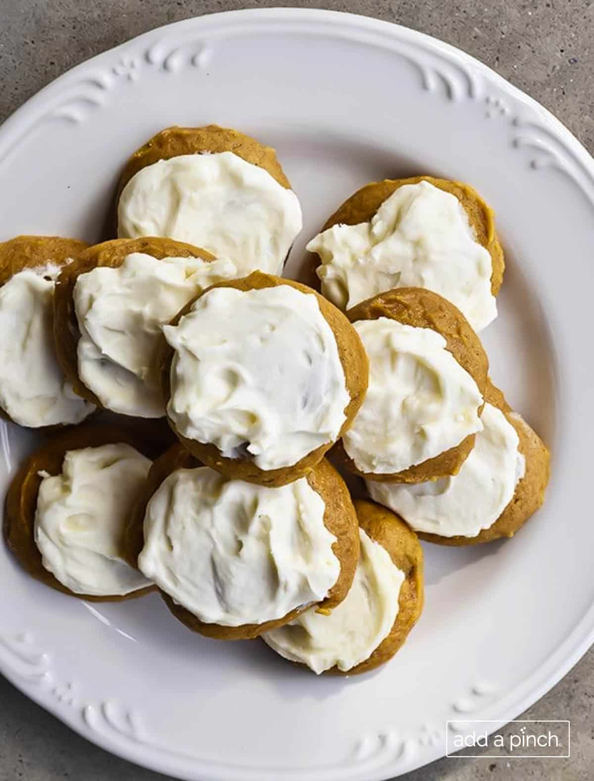 Photograph of frosted pumpkin cookies on a white plate for serving. 