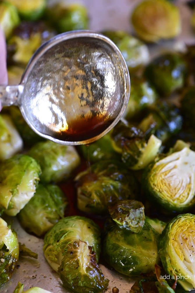 Brussels sprouts on pan after they are roasted, now being drizzled with maple syrup and balsamic vinegar. // addapinch.com