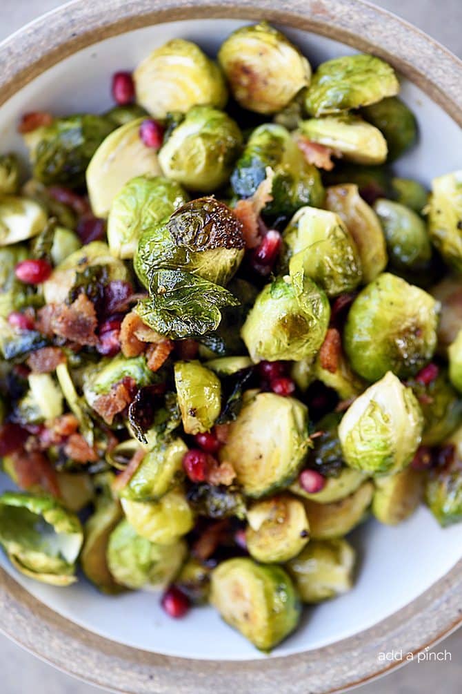Crispy Brussels Sprouts with Pomegranate and Bacon in a white serving bowl // addapinch.com