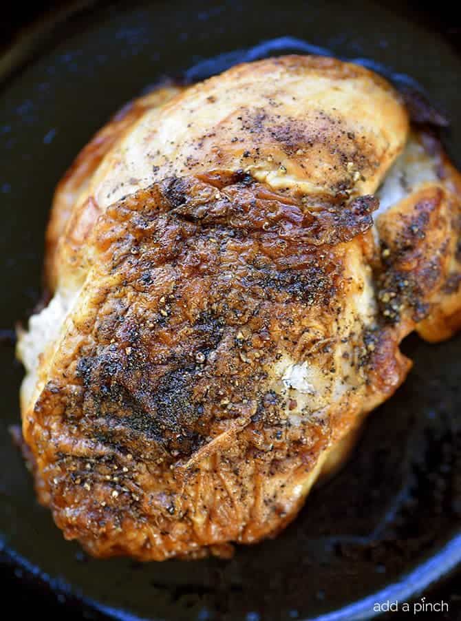 Photo of a roast turkey breast with a crispy, golden skin made is cooked in a cast iron skillet. 