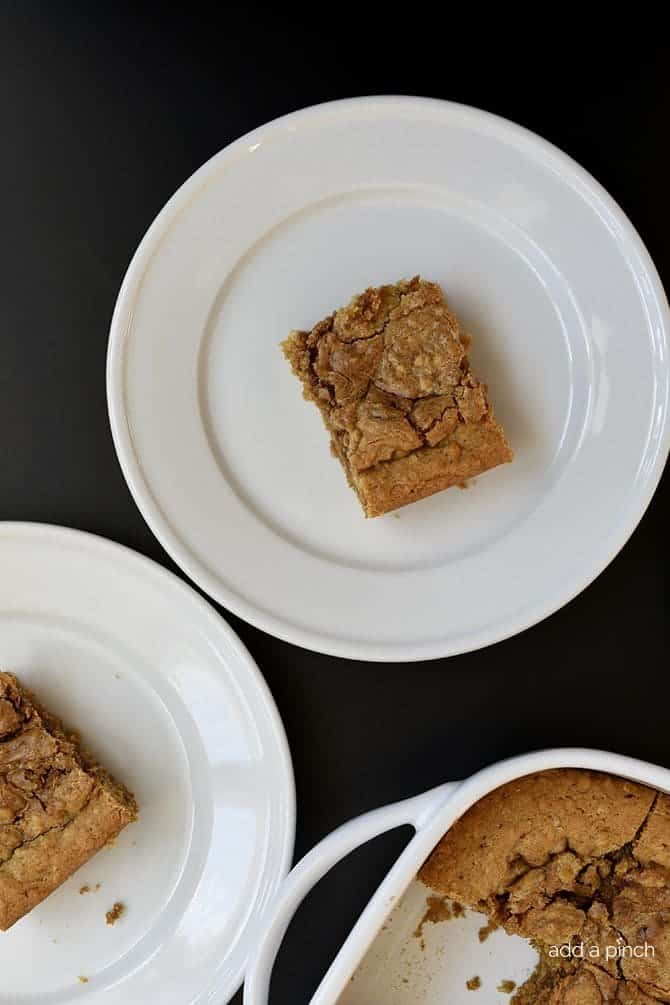 White plates with cinnamon swirl blondies on them and a baking dish filled with them on the side. 