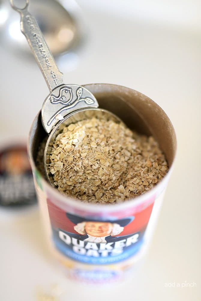 Measuring cup in a canister of quick-cooking oats on a white counter.