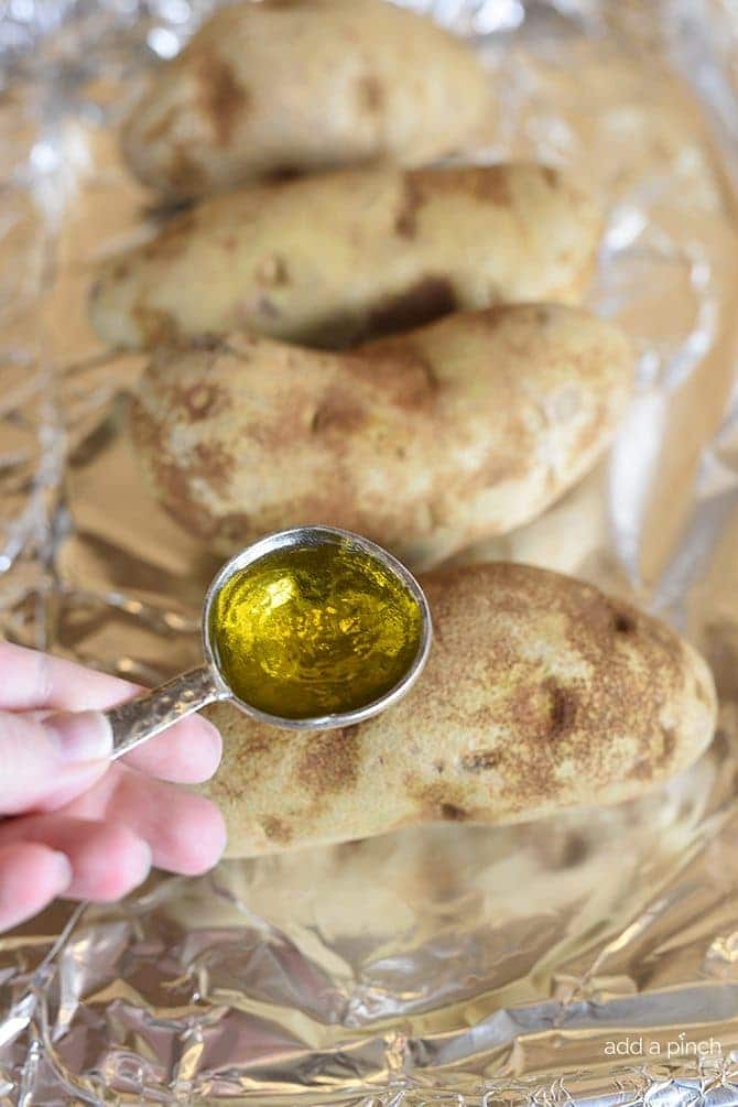 Clean russet potatoes on a foil-lined baking sheet, with a tablespoon of olive oil to rub onto a potato.  // addapinch.com