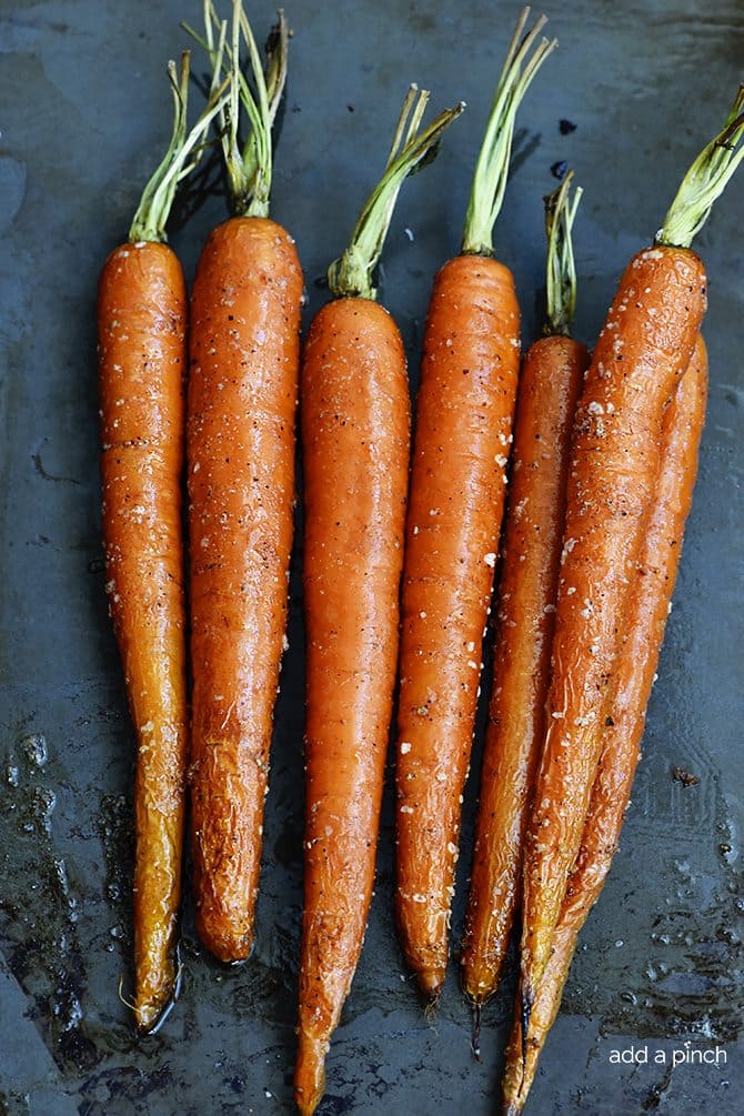 A baking pan holds several salted roasted carrots with green tops.