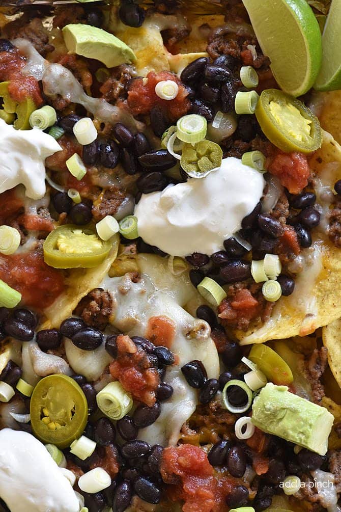 Close up of nachos with cheese, sour cream, black beans, salsa, avocado onion and jalapenos. // addapinch.com
