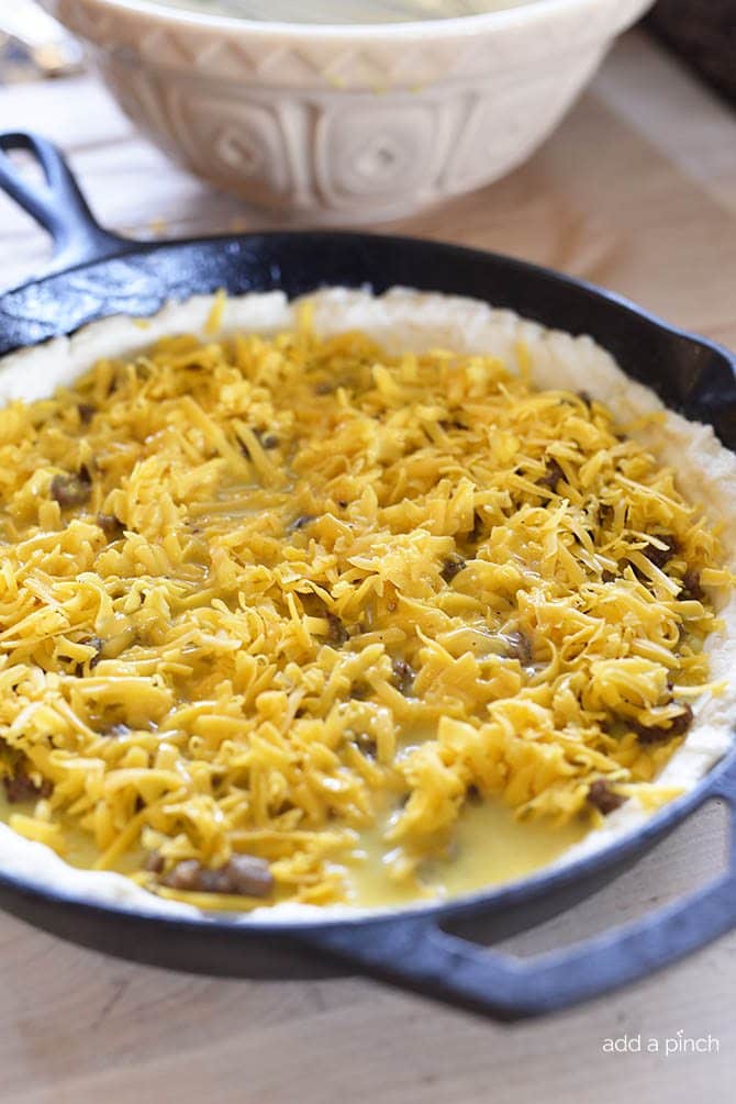 Shredded cheese tops egg mixture and browned sausage on a biscuit crust in an iron skillet // addapinch.com