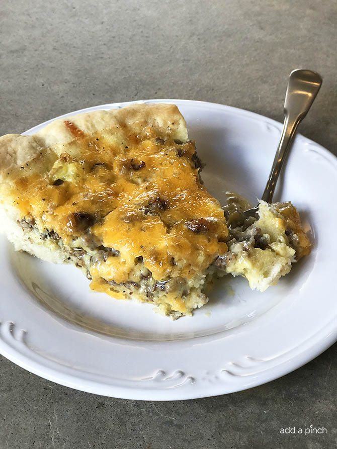 Slice of quiche with sausage and cheese on a white plate with a fork // addapinch.com