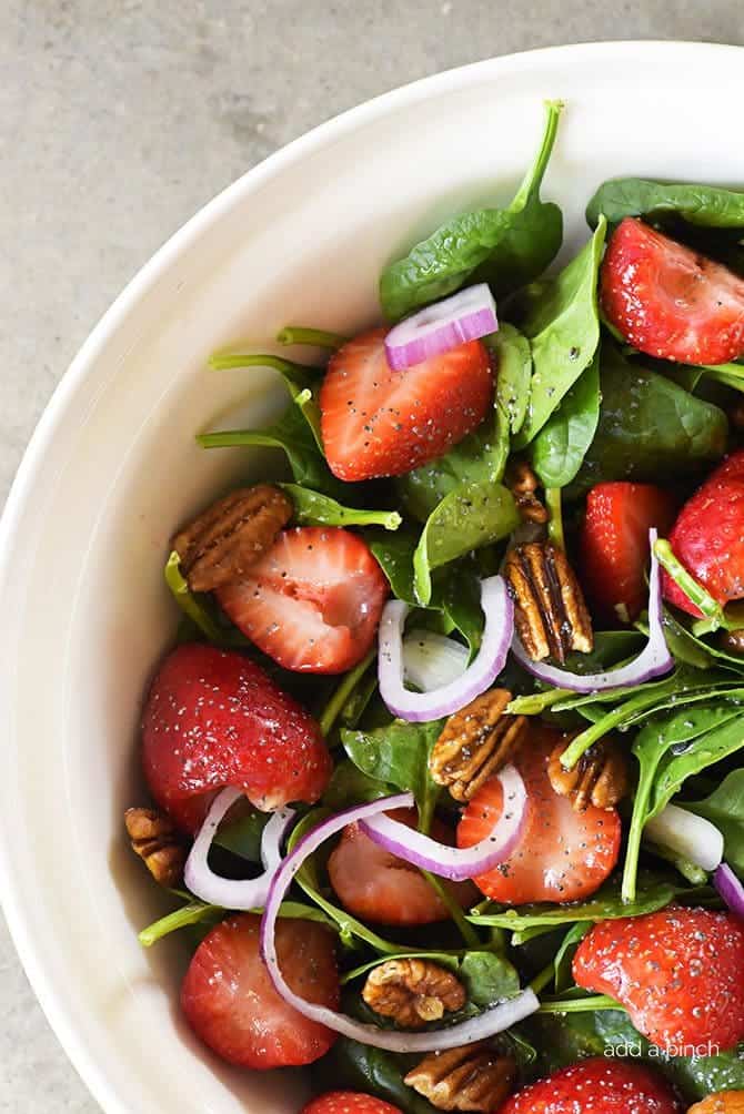 Photograph of fresh salad made with spinach, strawberries, toasted pecans, red onion, and tossed with a poppy seed dressing. / addapinch.com

#springsalad #strawberryspinachsalad #addapinchrecipes #saladrecipes