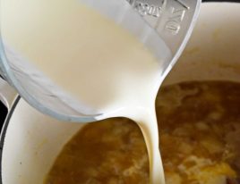 Photo of heavy cream being added to a Dutch oven of soup.