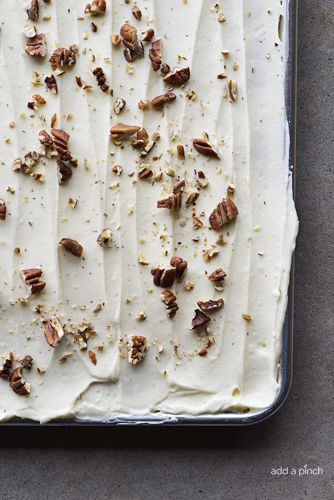 Carrot cake sheet cake with cream cheese frosting and toasted pecan pieces on gray background.
