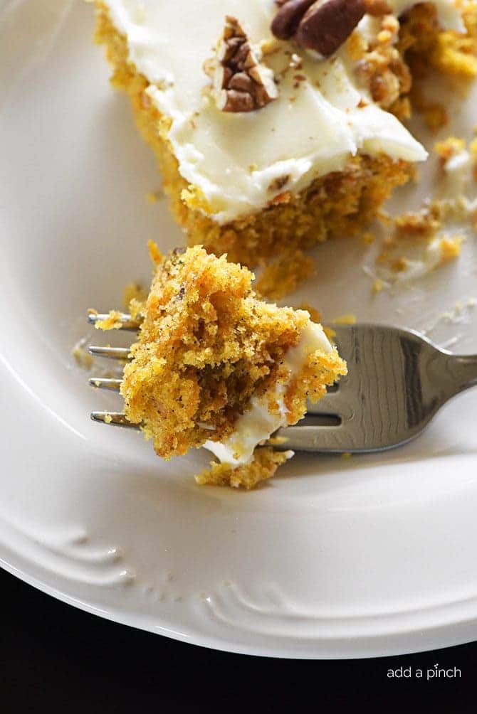 Bite of carrot cake on a fork with larger piece of cake in the background. | addapinch.com