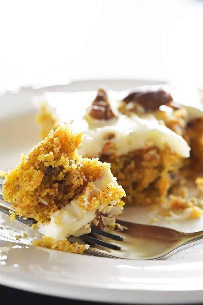 Bite of carrot cake topped with cream cheese frosting on a fork on a white plate. | addapinch.com