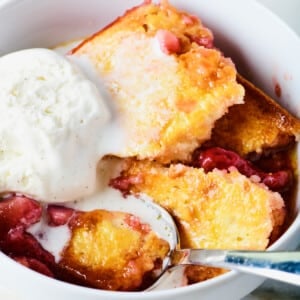 Strawberry cobbler in a white bowl with vanilla ice cream and a spoon.