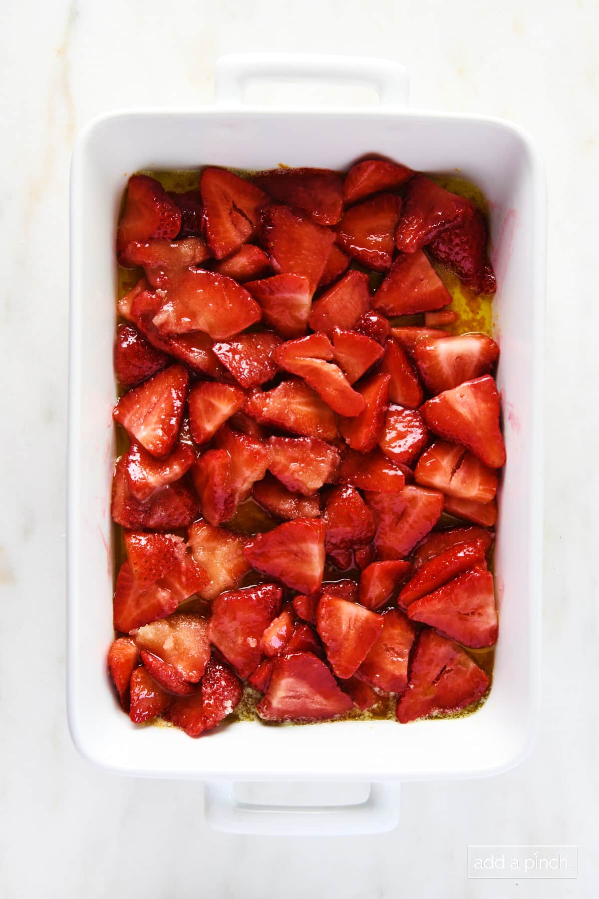 Sliced strawberries poured over butter in a white baking dish