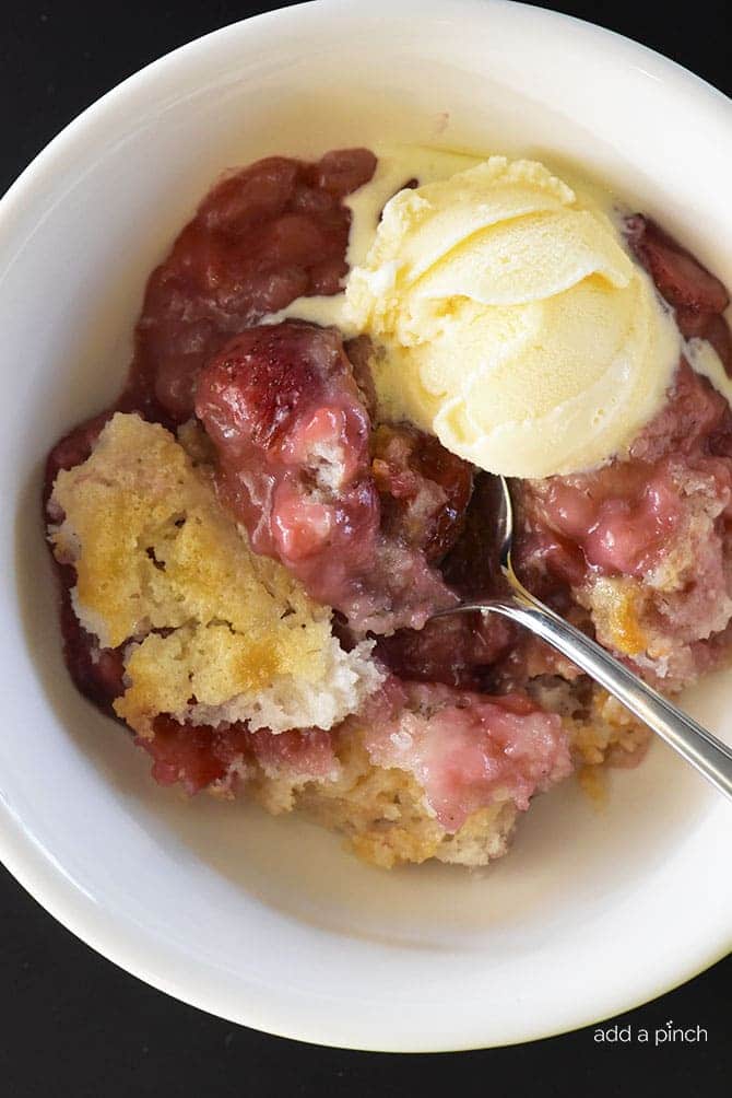 Strawberry Cobbler in white bowl, with spoon and scoop of vanilla ice cream. // addapinch.com