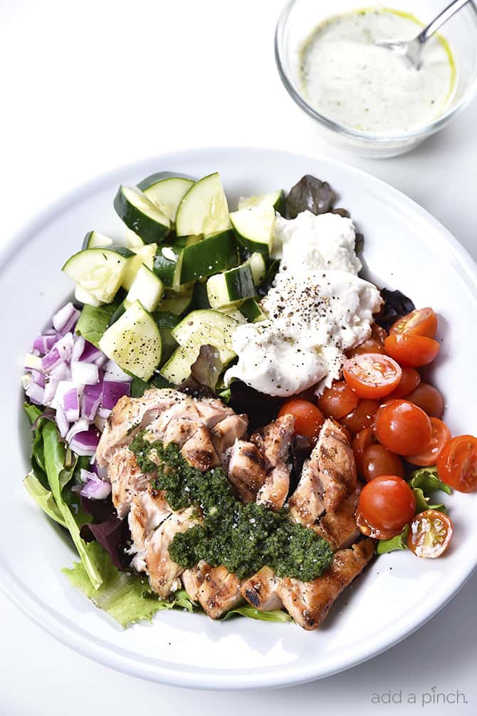  Grilled Chicken Salad with Pesto Ranch Dressing Recipe makes a delicious salad with cucumbers, tomatoes, onion, mozzarella topped with grilled chicken and a pesto ranch dressing! // addapinch.com