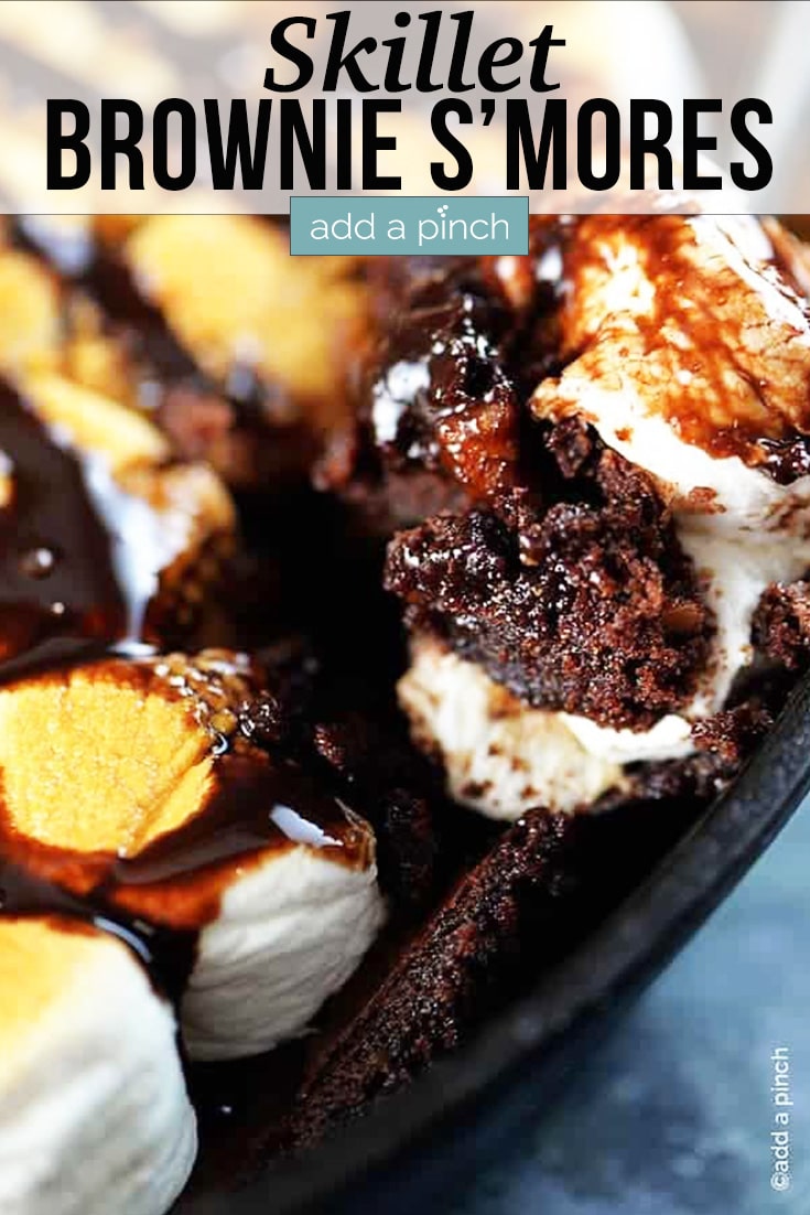 Skillet Brownie S'mores in an iron skillet with brownie topped with toasted marshmallows and drizzled with chocolate - with text - addapinch.com