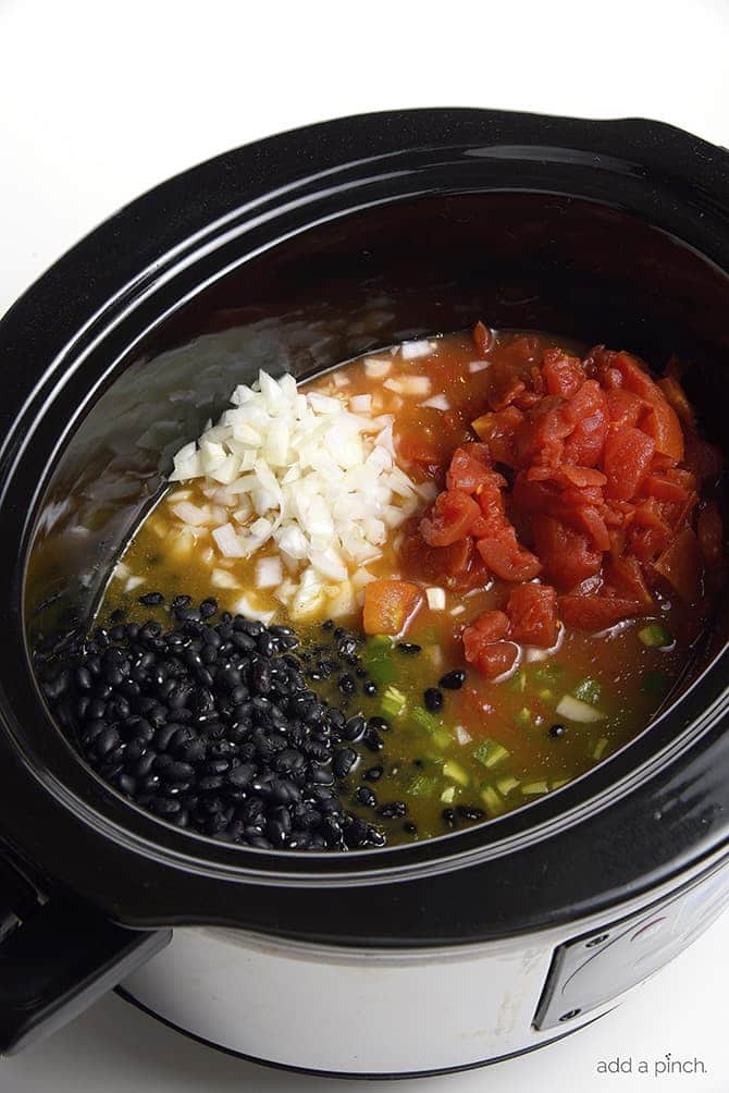 Slow cooker filled with ingredients for black bean soup // addapinch.com