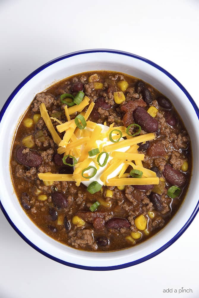 Bowl of meaty soup in a white bowl with blue rim topped with sour cream, shredded cheddar cheese, and sliced green onions. 