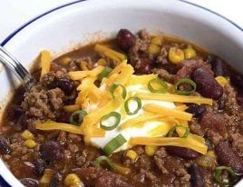 Taco Soup in a white bowl topped with sour cream, cheese, and green onions. #tacosoup #kidfriendly