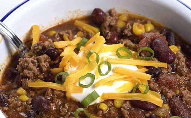 Taco Soup in a white bowl topped with sour cream, cheese, and green onions. #tacosoup #kidfriendly
